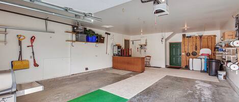 Een ruime garage met een betonnen vloer, een groen vloerkleed en diverse gereedschappen en apparatuur.