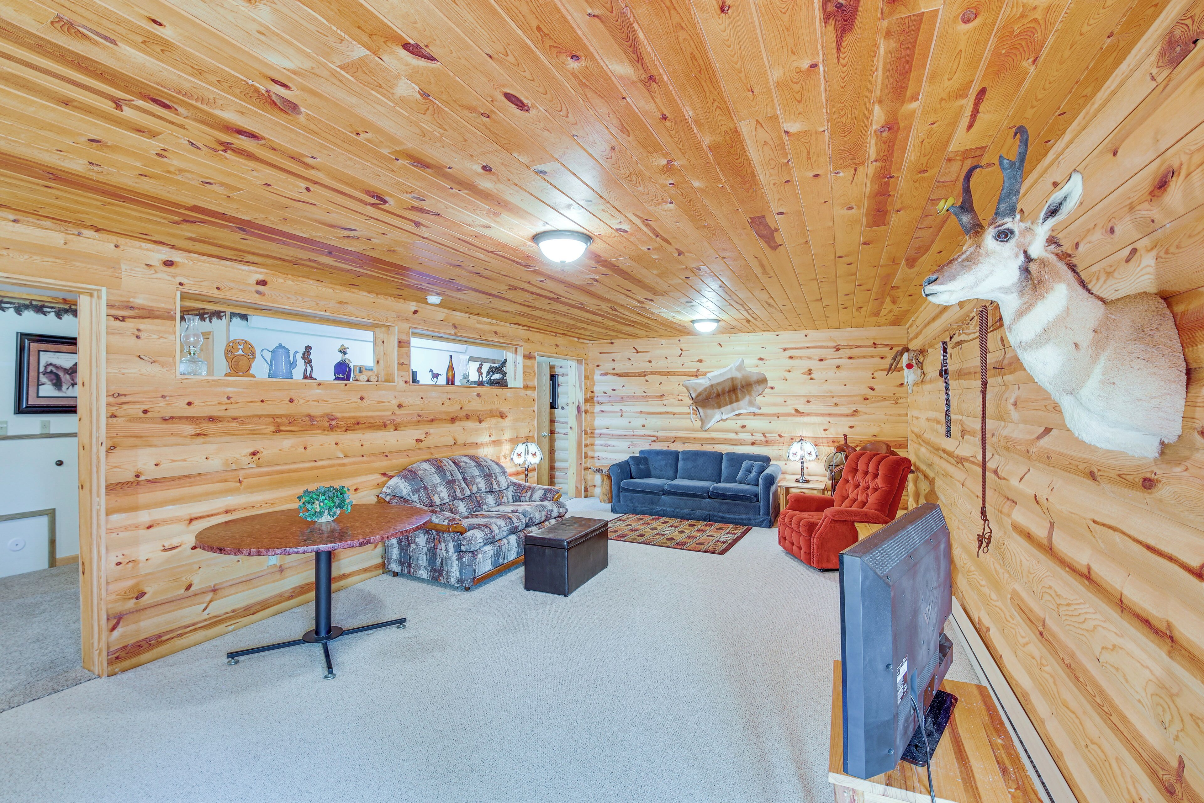 L’intérieur d’une cabane en rondins, avec une table ronde, deux canapés, un téléviseur et une tête d’animal fixée au mur.