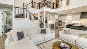 A spacious living area with a high ceiling, a staircase, and a kitchen area. - Hot Tub, Fire Pit! High-end Cedar Creek Lake Haven (Mabank)