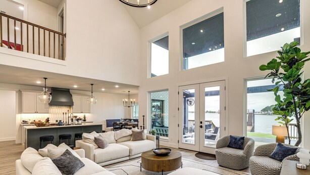 A spacious living area with a high ceiling, a kitchen with a bar, and a view of the outdoors. - Hot Tub, Fire Pit! High-end Cedar Creek Lake Haven (Mabank)
