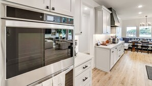A modern kitchen with white cabinetry, a large oven, and a dining area with a table and chairs. - Hot Tub, Fire Pit! High-end Cedar Creek Lake Haven (Mabank)