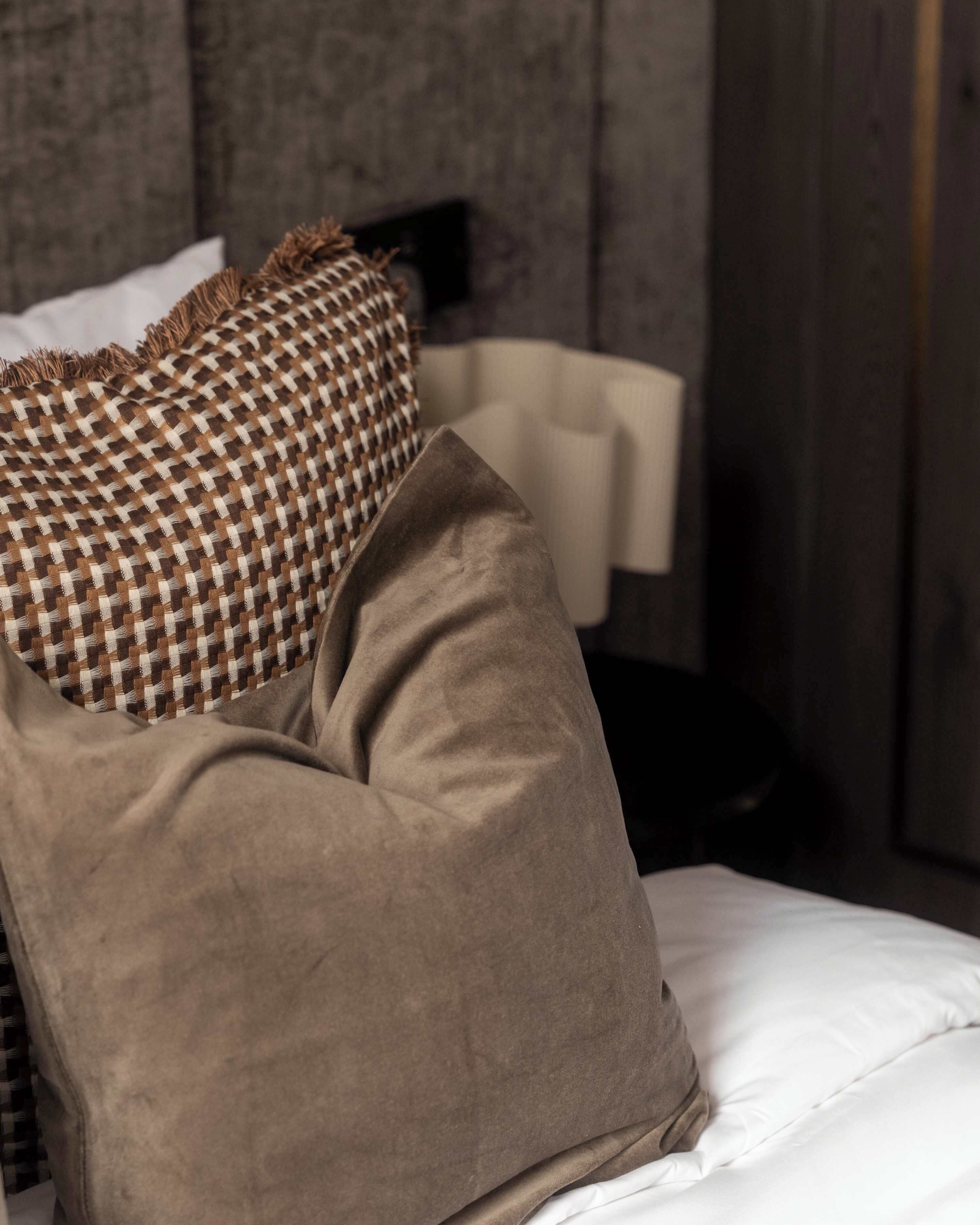 A bed with a checkered pillow and a plain pillow, a white sheet, and a wooden headboard.