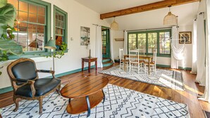 A dining area with a wooden table and chairs, a patterned rug, and a large window with green shutters. - Walkable Location: Historic Home in Charles Town! (Charles Town)