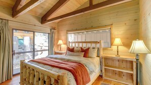 Un dormitorio de cabaña de madera con una cama, dos mesitas de noche y un ventanal grande.