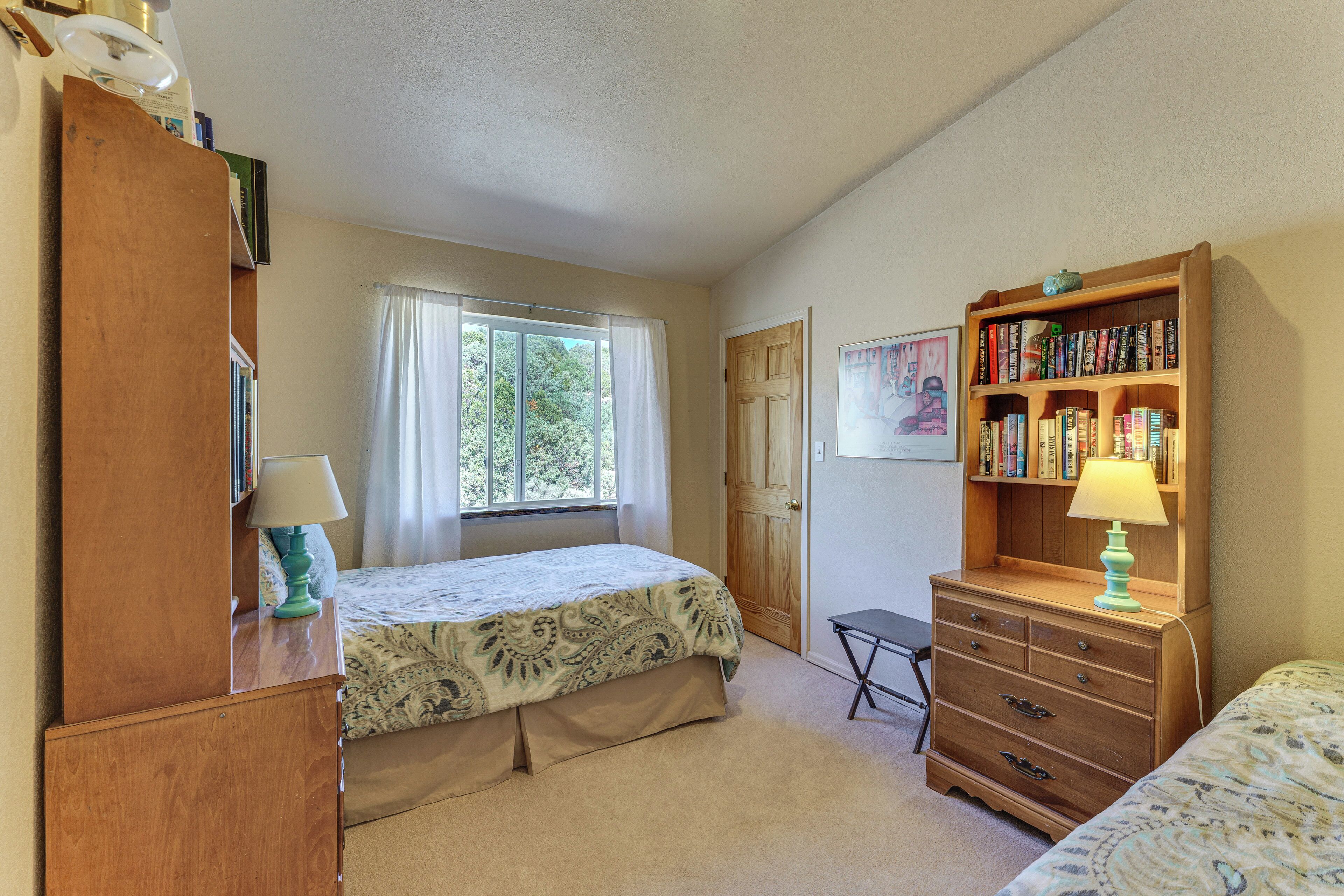 A bedroom with a bed, a dresser, a bookshelf, a window with curtains, and a door.