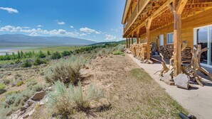 A wooden building with a covered porch, a view of mountains, and a dry landscape with sparse vegetation. - Walk to Lake: Scenic Southern Colorado Escape! (San Luis)