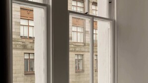 Blick durch ein Fenster mit weißem Rahmen auf ein Gebäude mit klassischer Architektur, darunter Rundbogenfenster und dekorative Stuckleisten.