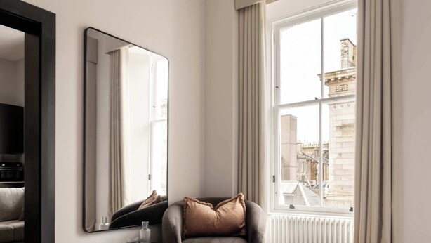 Ein modernes Hotelzimmer mit großem Fenster, einem Sessel, einem runden Beistelltisch und einem Bett.
