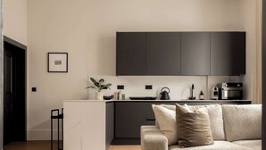 Ein modernes Wohnzimmer mit einer Couch und einer Küchenzeile mit dunklen Schränken und einer Marmorarbeitsplatte.