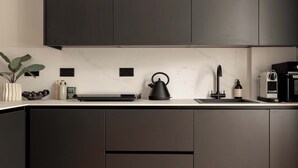Eine moderne Küche mit dunklen Schränken, einer Marmorarbeitsplatte, einem Wasserkocher, einer Kaffeemaschine und einem Spülbecken.
