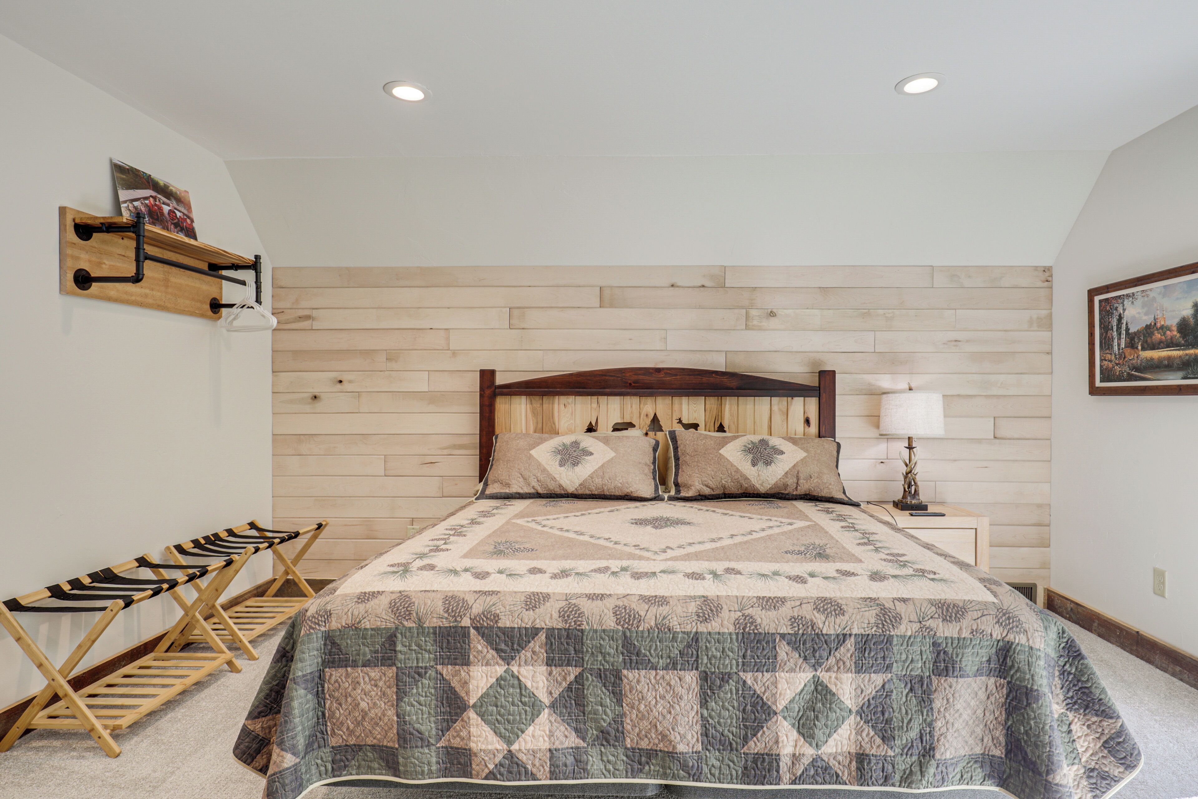 A bedroom with a wooden headboard, a quilted bedspread, a wooden bench with a hanging rack, and a nightstand with a lamp.