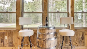 A rustic wooden room with large windows, two white bar stools, and a wooden barrel with a bottle on top. - 3 MI to Lake: Pet Friendly Wabeno Cabin! (Wabeno)