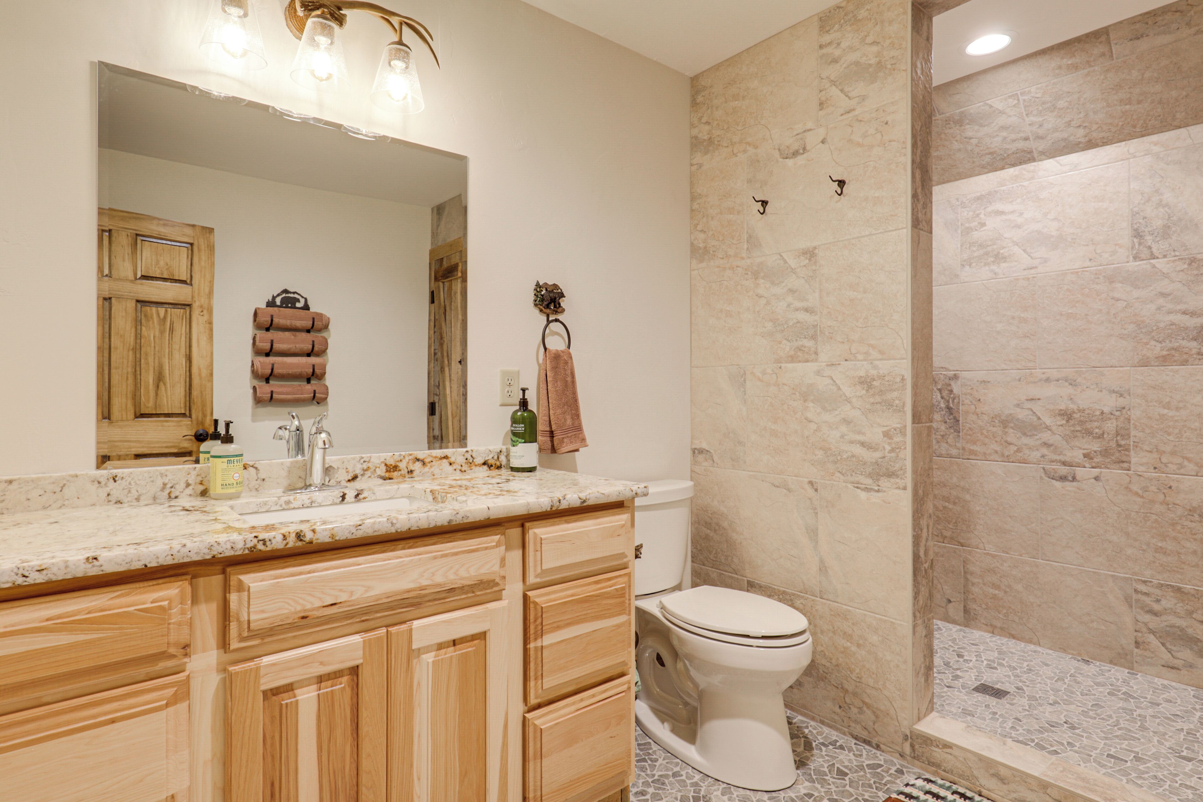 A bathroom with a wooden vanity, a large mirror, a towel rack, and a shower area with tiled walls.