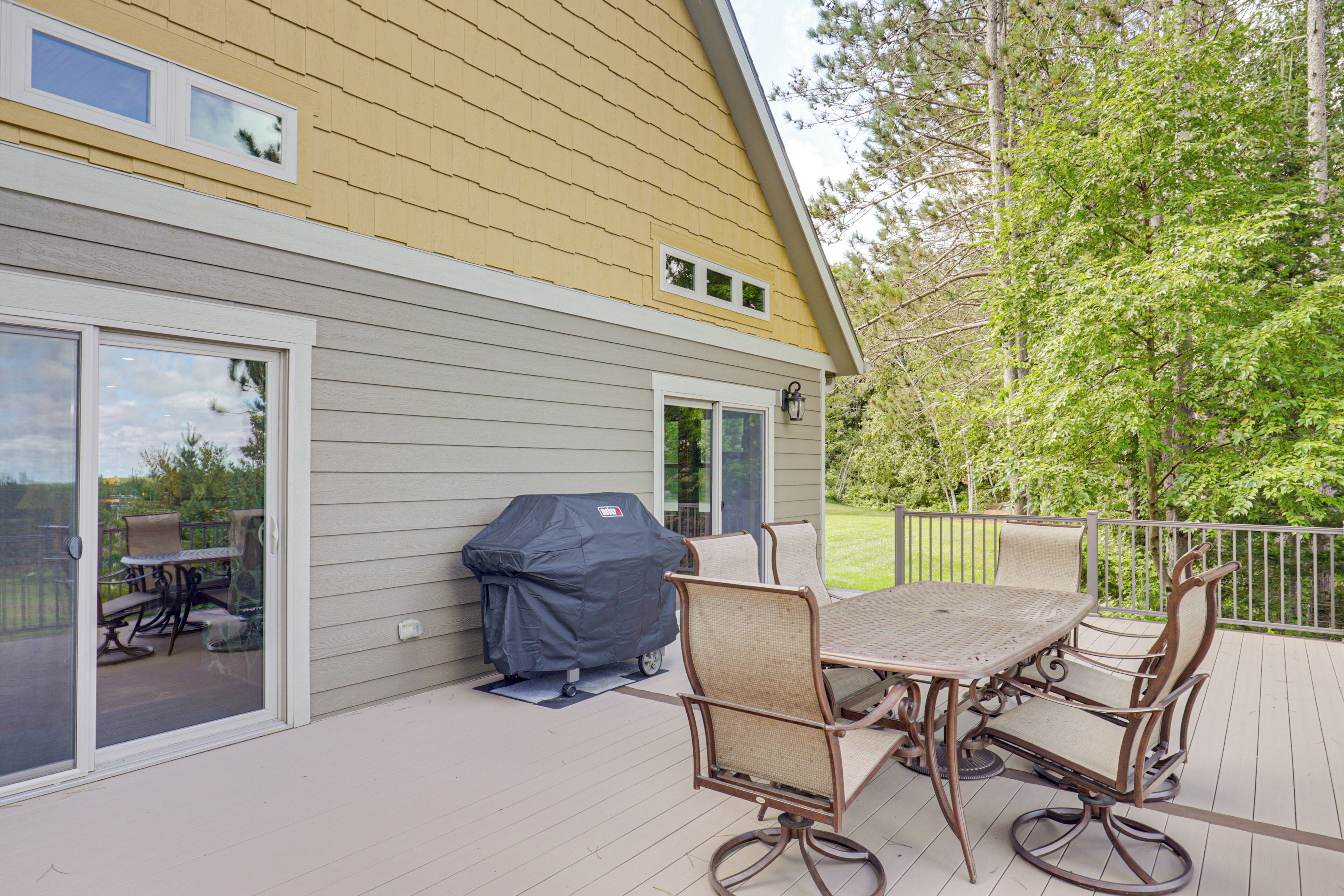 An outdoor patio with a covered grill, a dining table with chairs, and a sliding glass door leading to a deck.