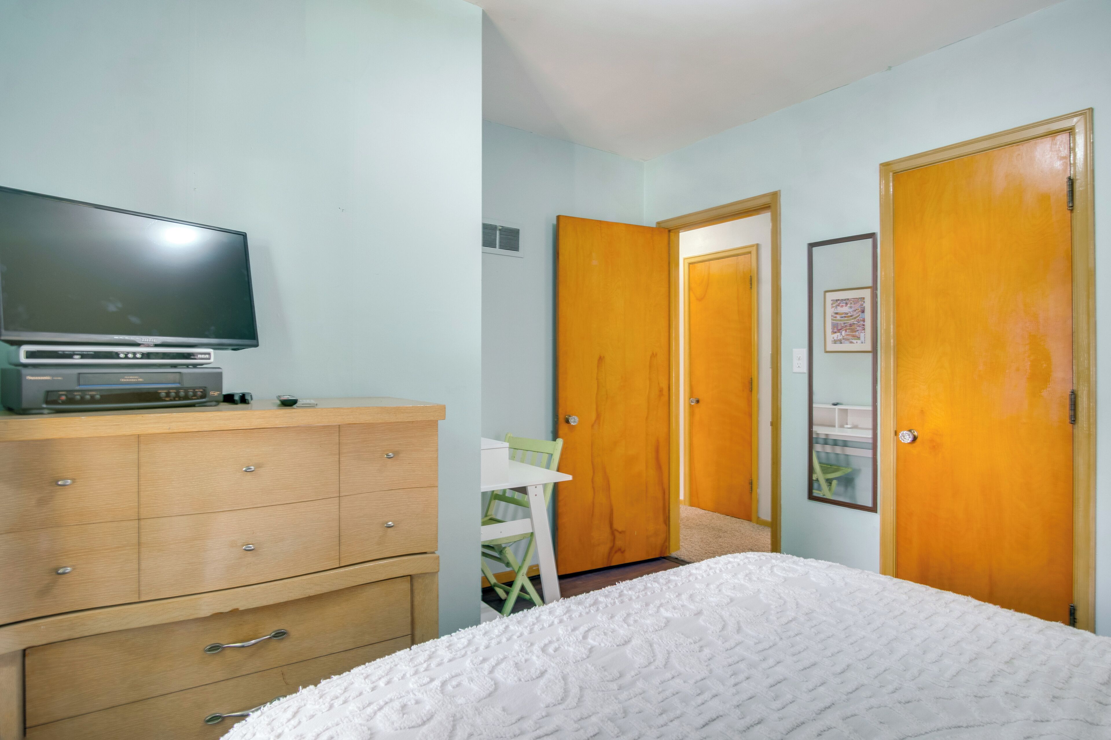 A bedroom with a bed, a dresser, a television, and two doors.