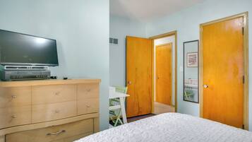 A bedroom with a bed, a dresser, a television, and two doors.
