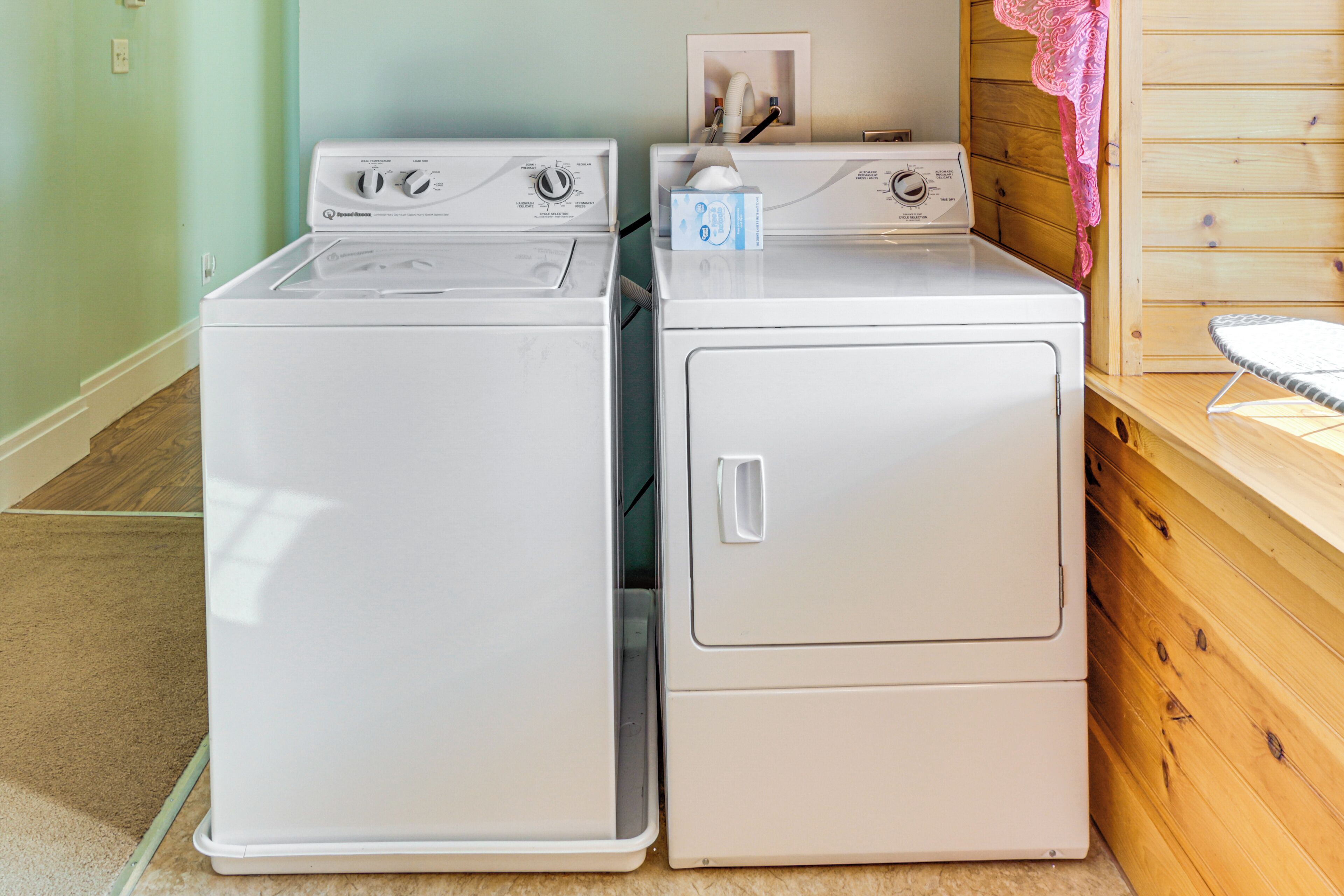 Two stacked front-loading washing machines in a laundry room with a wooden wall and a towel rack.