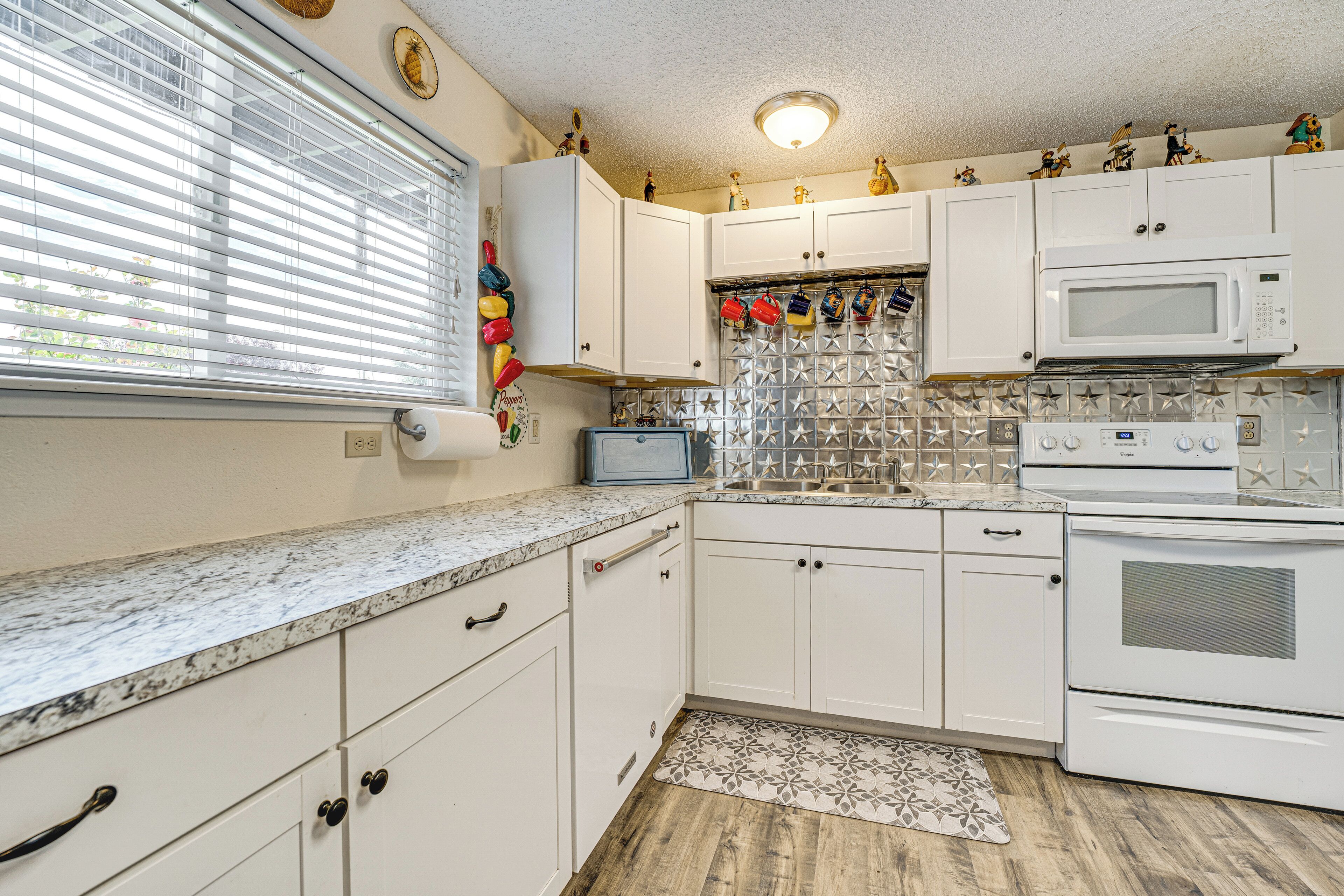 A kitchen with white cabinets, a microwave, a stove, and a window with blinds.