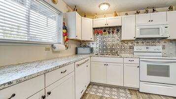 A kitchen with white cabinets, a microwave, a stove, and a window with blinds.