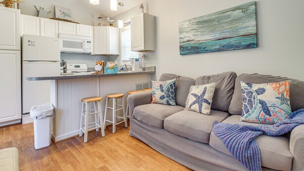 A modern kitchen with white cabinets, a microwave, and a coffee maker. There is a gray sofa with colorful pillows and a blanket. A painting hangs on the wall above the sofa. - 3 Mi to Icw: Coastal Carolina Home w/ Pool Access (Hampstead)