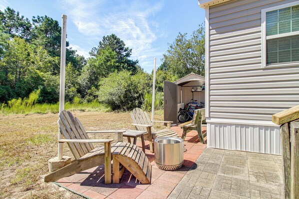 A patio with Adirondack chairs, a metal trash can, and a wooden shed.