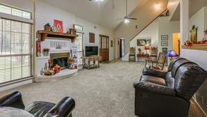 A spacious living room with a fireplace, a television, and a ceiling fan. - Relax By the Lake: Quiet East Texas Retreat (Village Mills)