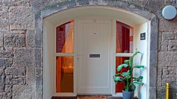 A stone building entrance with a white door, a potted plant, and a sign indicating a hotel.