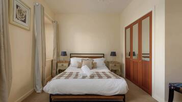 A neatly made bed with a checkered bedspread, two bedside lamps, a wooden wardrobe, and a framed picture on the wall.
