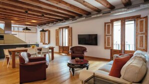 Amplia sala de estar con vigas de madera, una mesa de comedor, un sofá y un televisor.