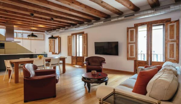A spacious living area with wooden beams, a dining table, a sofa, and a TV.