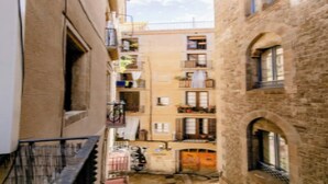 Un estrecho callejón entre edificios con balcones, una bicicleta y una puerta.