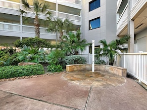 A courtyard with a stone fountain, palm trees, and a multi-story building with balconies.