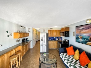 Un espacio habitable compacto con kitchenette, comedor y zona de estar con sofá y mesa de centro.