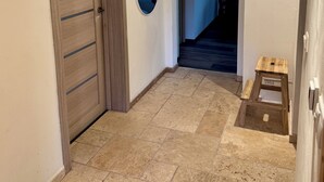 Un couloir avec une porte en bois, un petit marchepied et un sol carrelé.