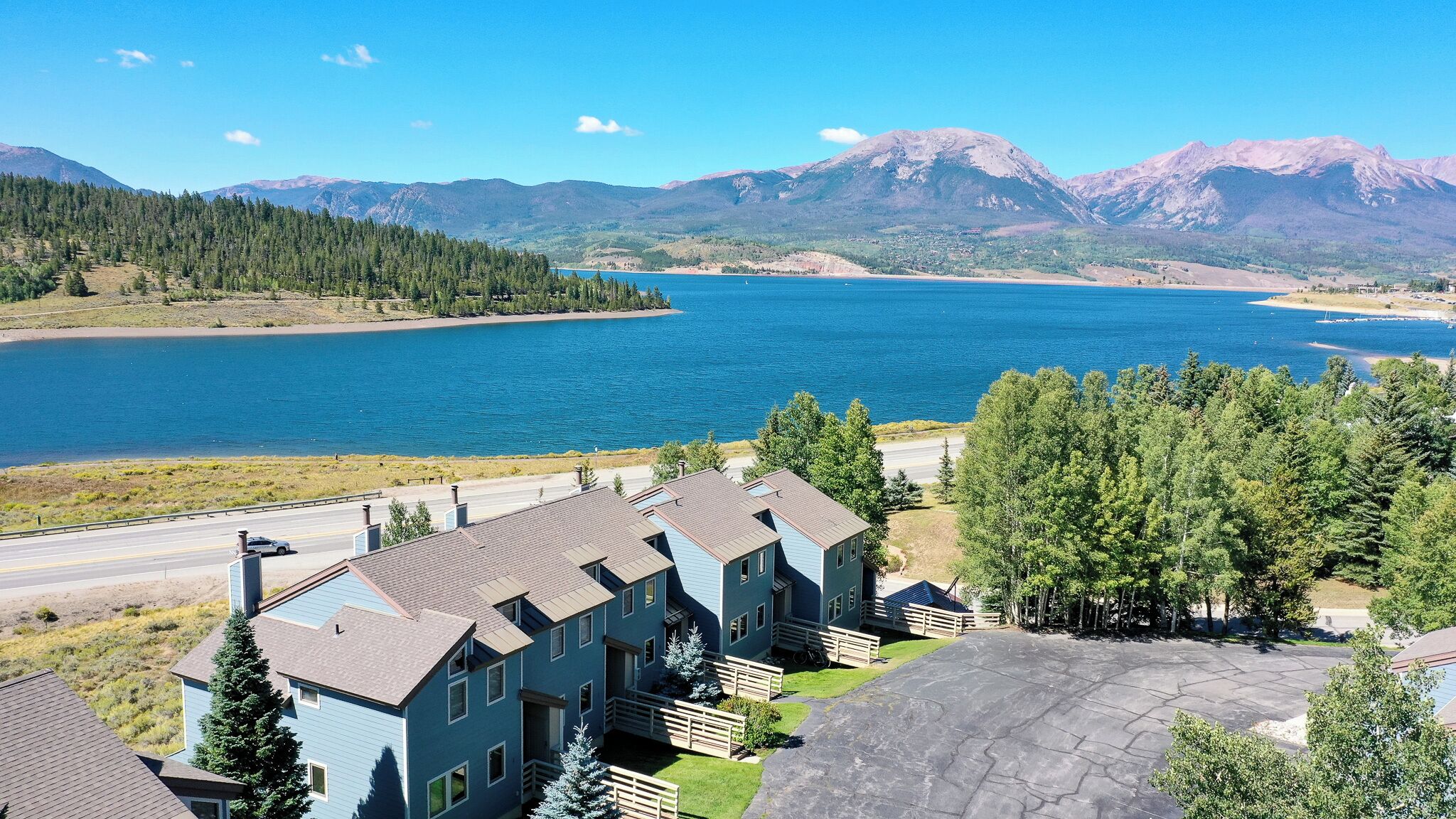 A residential area with a large house featuring a spacious driveway and a view of a lake and mountains.