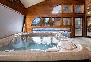 A hot tub in a room with wooden walls and large windows.