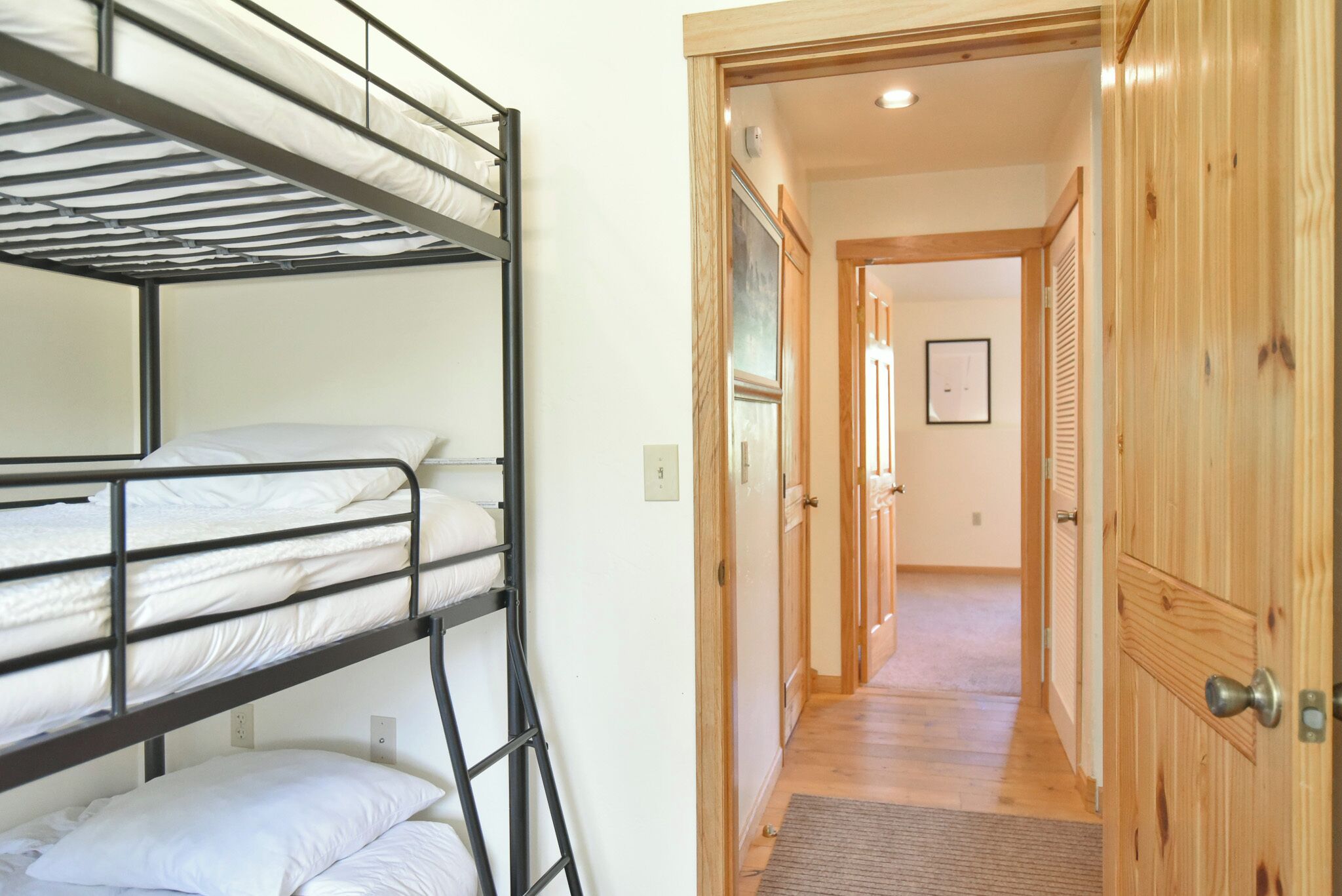 Habitación con literas, una puerta de madera y un pasillo que conduce a otra habitación.