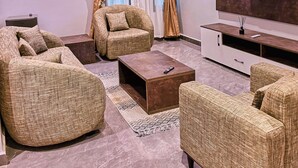A modern living room with a flat-screen TV, two sofas, a coffee table, and a large window with curtains. - Saint Tropez Hotel and Suites (Abuja)