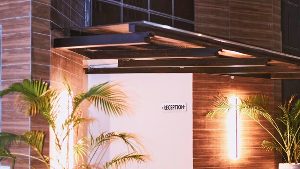 A reception area with a sign, potted plants, and a modern building facade. - Saint Tropez Hotel and Suites (Abuja)