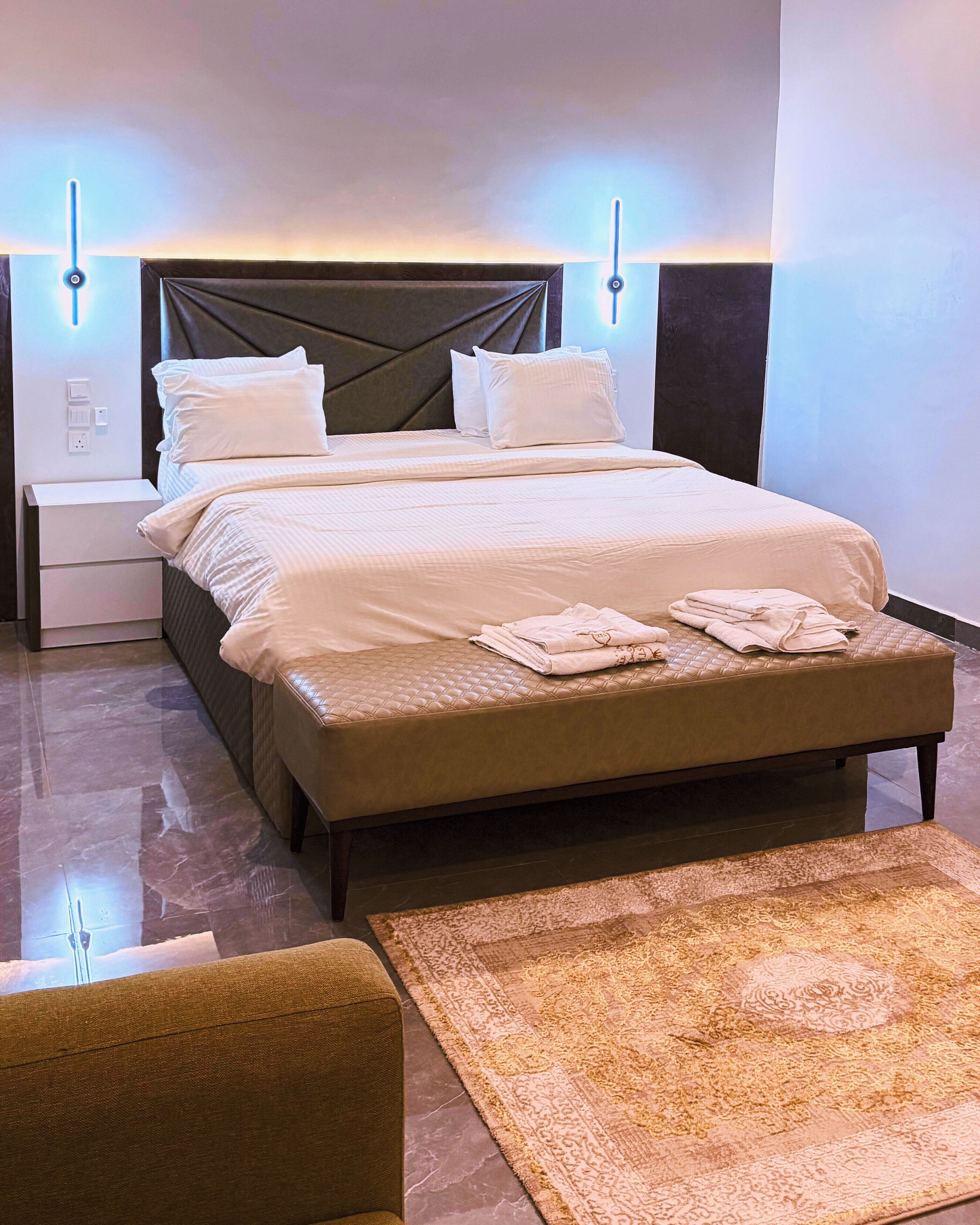 A neatly made bed with a quilted headboard, a bedside table with a lamp, and a patterned rug on the floor.