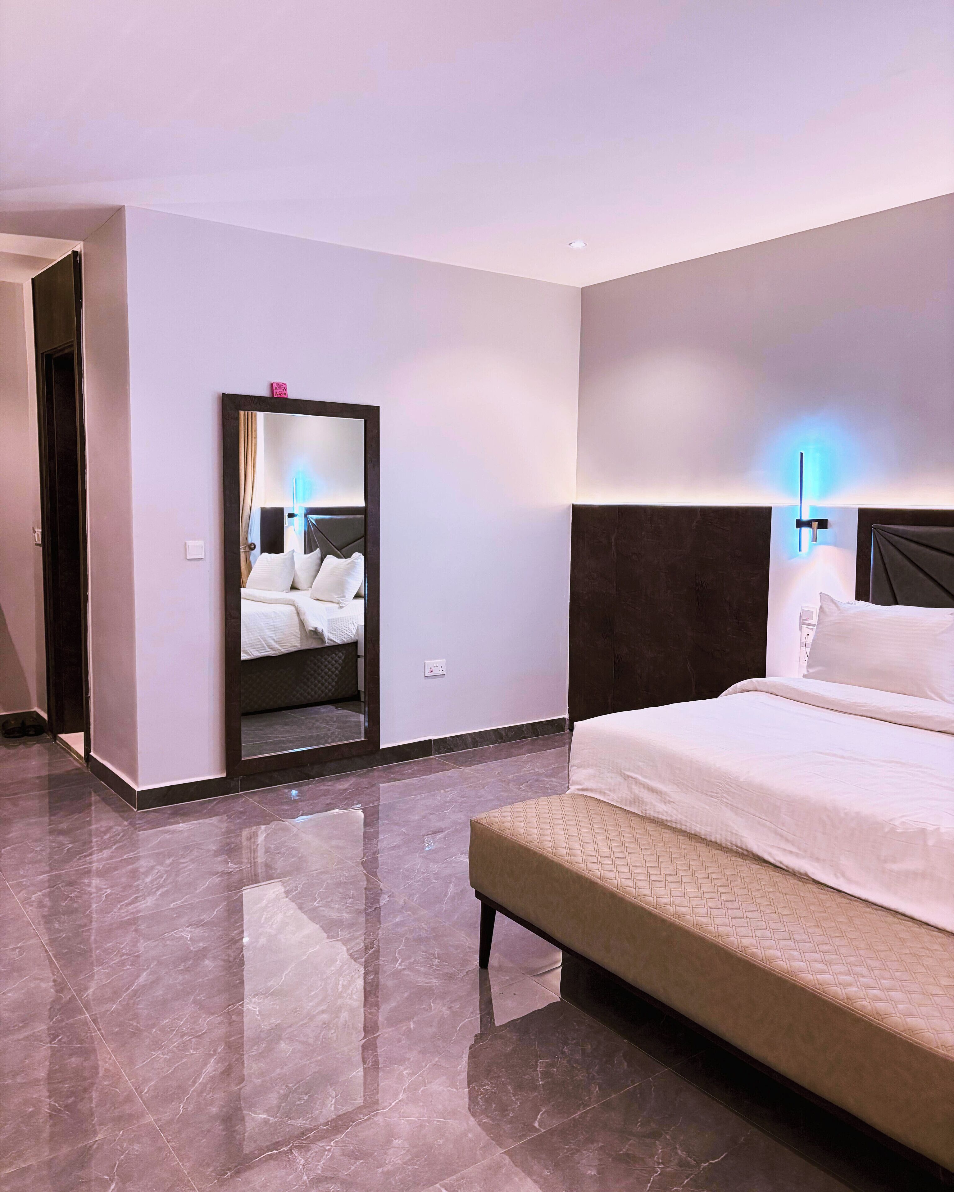 A modern hotel room with a large bed, a mirror, and a dark headboard.