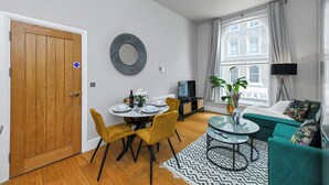 A compact living space with a dining area, a sofa set, and a view of a building through a window. - Market Street Apartment 3A Flat 1 (Nottingham)