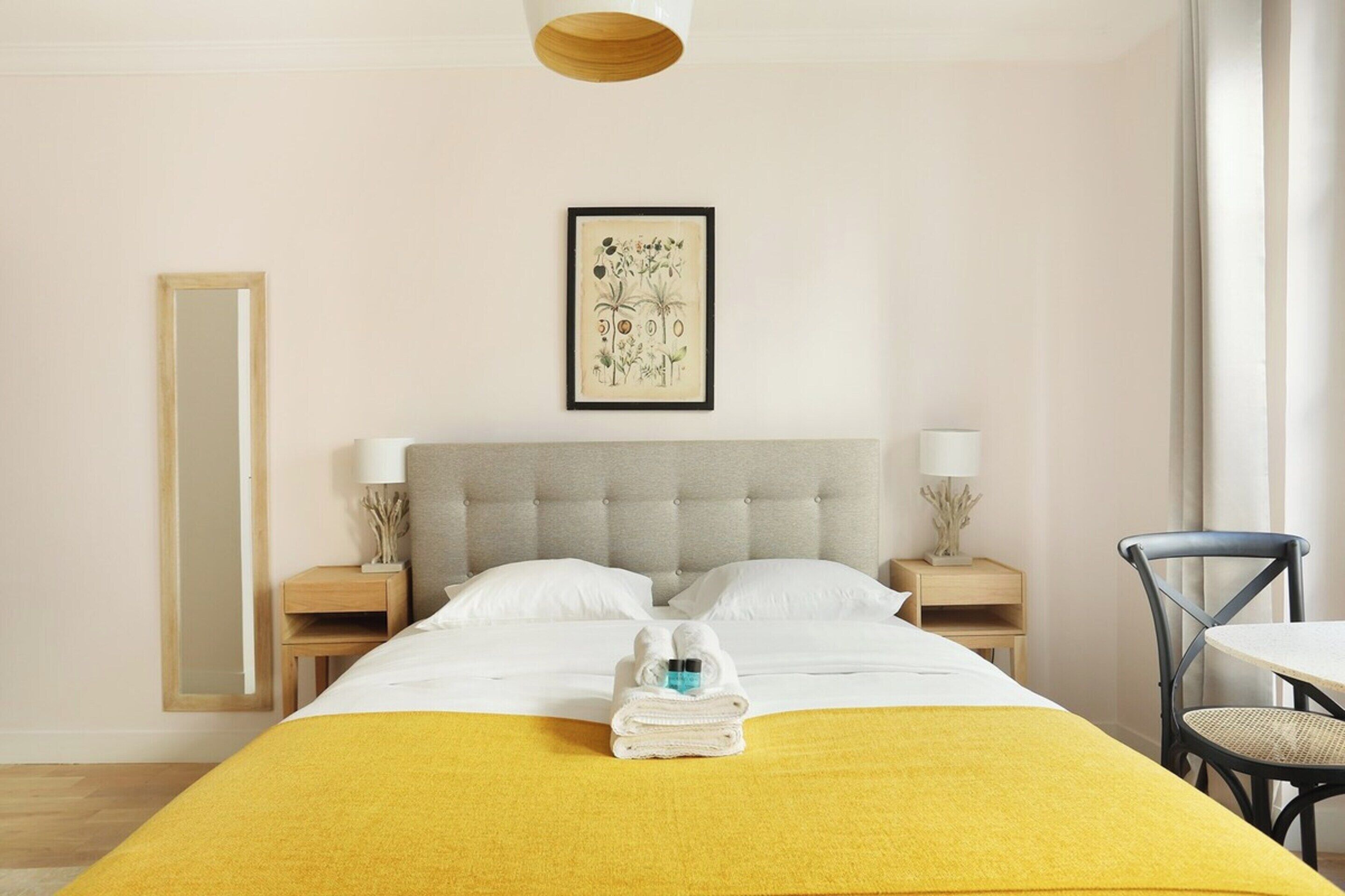 Une chambre d’hôtel avec un lit, une table de chevet avec une lampe, une chaise et une œuvre d’art encadrée au mur.