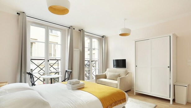 Ein Hotelzimmer mit Bett, Sofa, Fernseher, Kleiderschrank und einem Balkon mit Tisch und Stühlen.