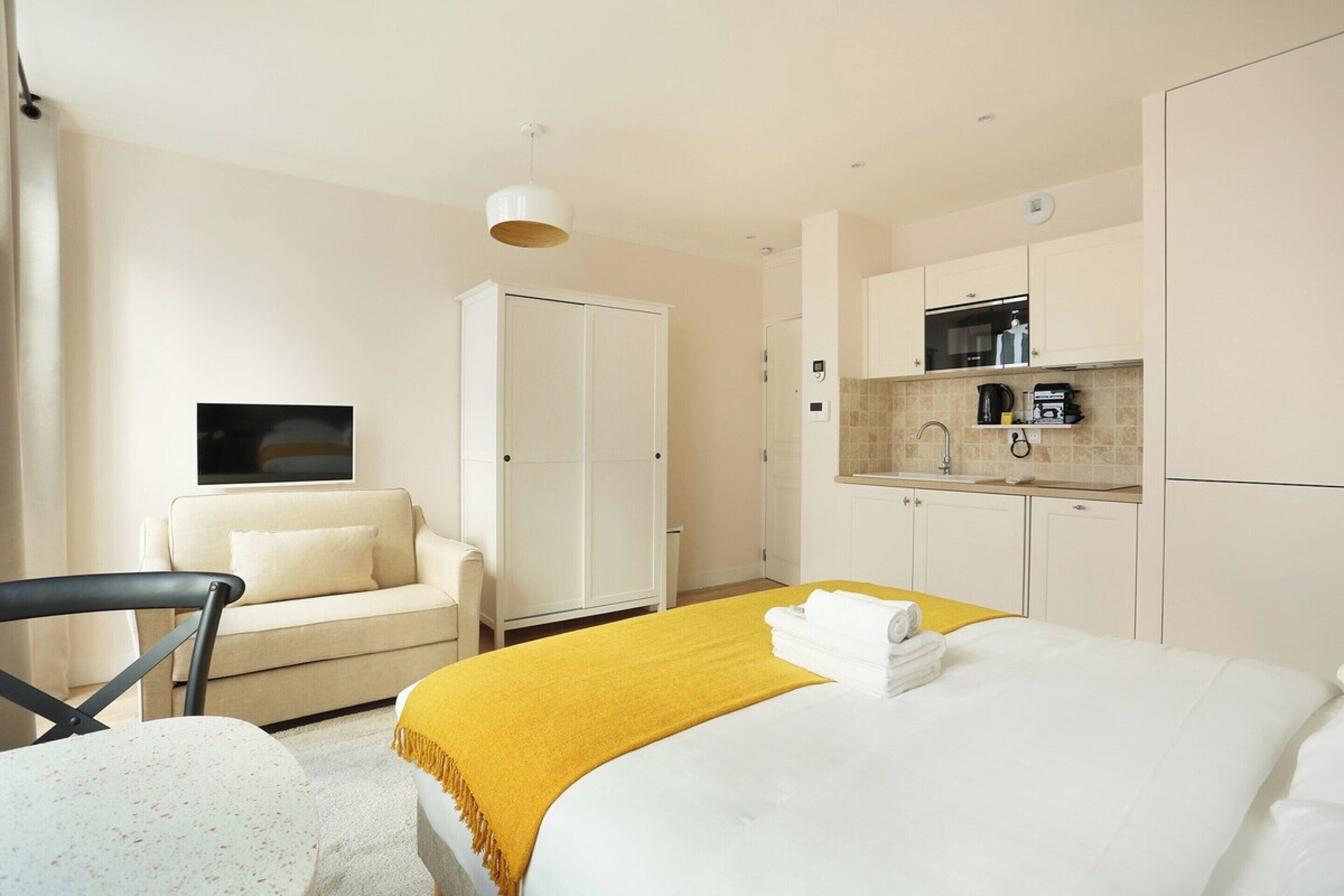 A hotel room with a bed, a sofa, a desk, and a kitchenette.