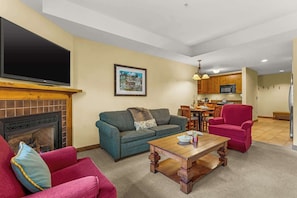 A living room with a fireplace, a television, a sofa, a coffee table, and a kitchen in the background. - Studio Deluxe in the Lodge at Mountaineer Square (Crested Butte)