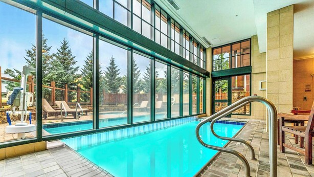 An indoor swimming pool with clear glass walls, a tiled floor, and a view of outdoor trees. - NEW LISTING | Studio at Mountaineer Square, Lifts 2 min Walk (Crested Butte)