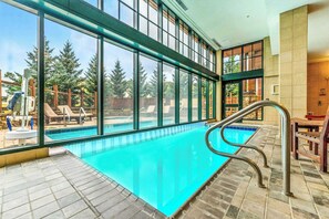 Ein Hallenbad mit großen Glaswänden, gefliestem Boden und Blick auf Bäume draußen.