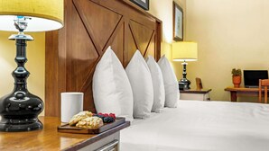 A hotel room with a wooden headboard, a bedside table with a lamp, a tray of snacks, and a bed with white bedding. - NEW LISTING | Studio at Mountaineer Square, Lifts 2 min Walk (Crested Butte)