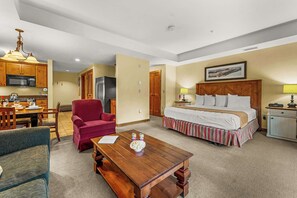 Ein Hotelzimmer mit einem Bett, einem Esstisch, einem roten Sessel, einem Holztisch, einer Mikrowelle, einem Kühlschrank und einer Lampe.